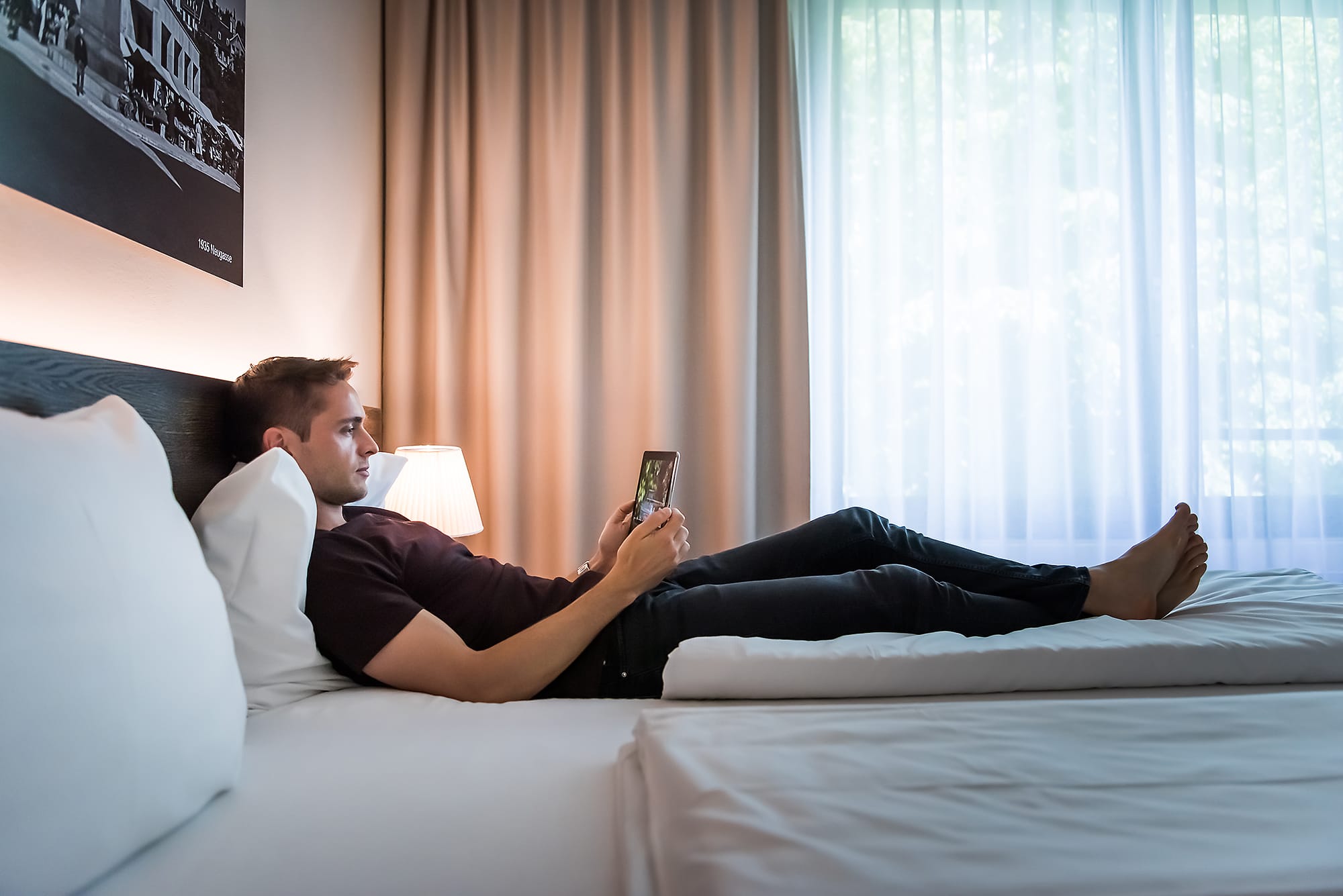 Gast liegt im Bett mit iPad, Hotel one66